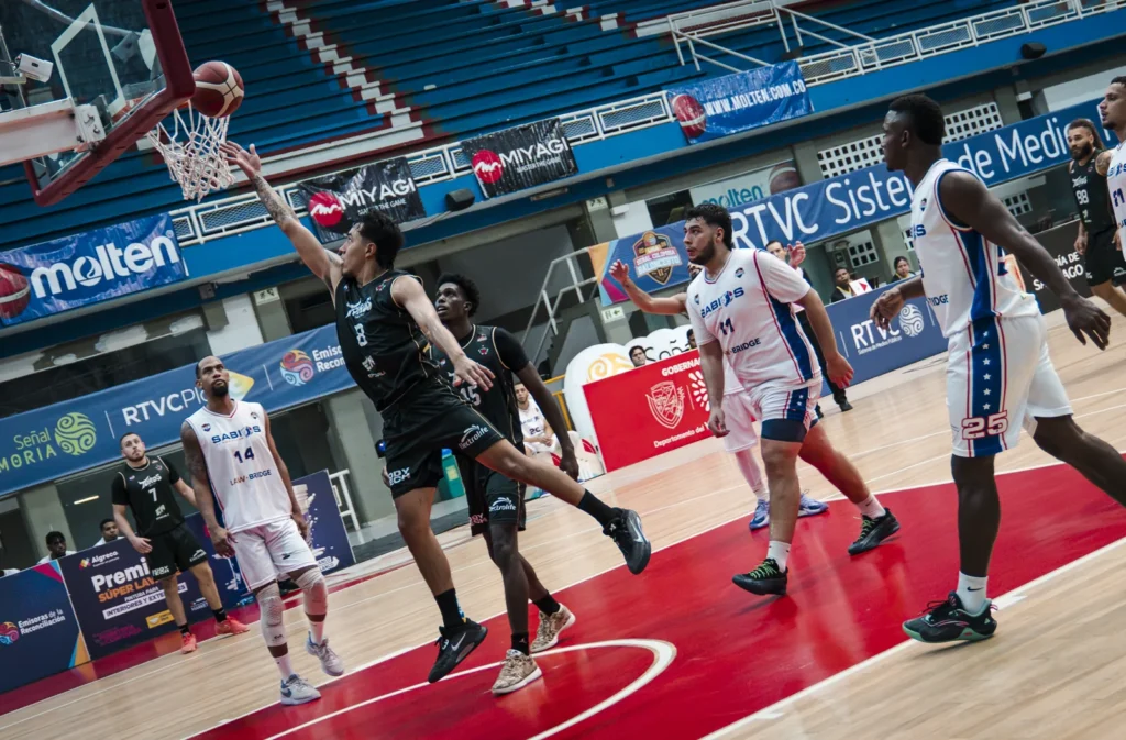 Jugador de Toros del Valle con uniforme negro ataca el aro con el balón ante la defensa de Sabios de Manizales