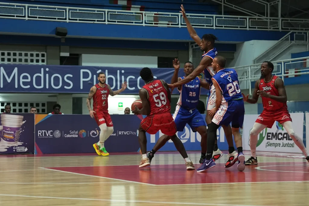 Hayner Montaño, #59 de Toros del Valle, protege el balón entre defensores de Sabios de Manizales