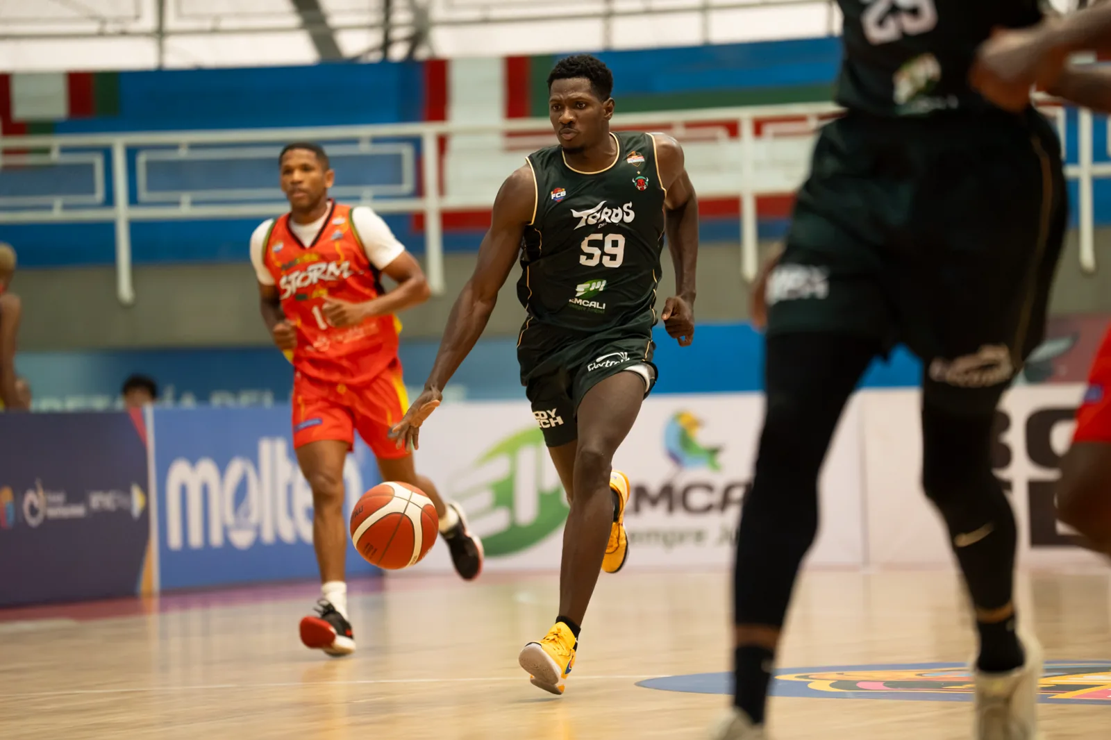 Hayner Montaño, #59 de Toros del Valle, conduce el balón en transición mientras un jugador de Caribbean Storm lo sigue